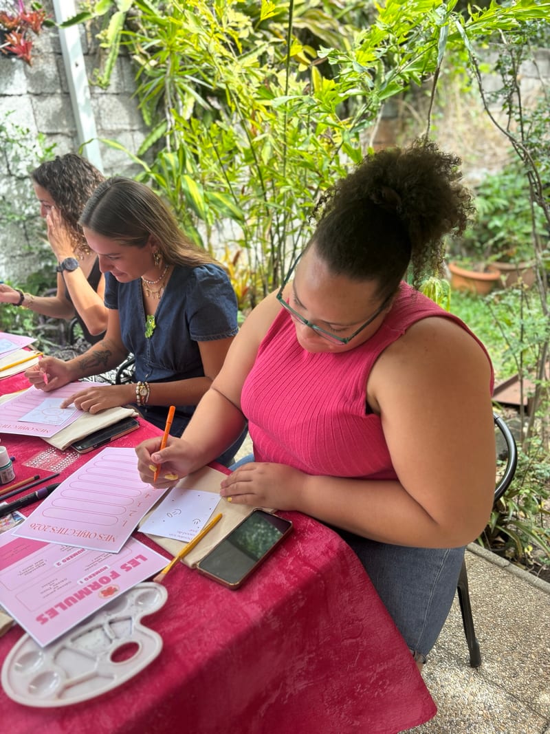 Participantes dessinant leurs motifs sur des tote bags, autour d’une table rose en plein air