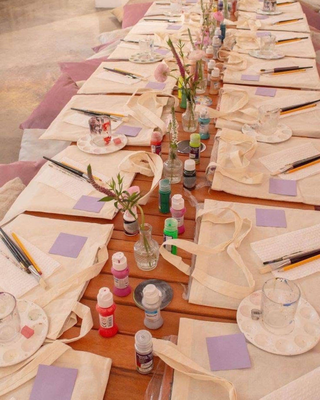 Table préparée avec des tote bags vierges, des pinceaux et de petits bouquets