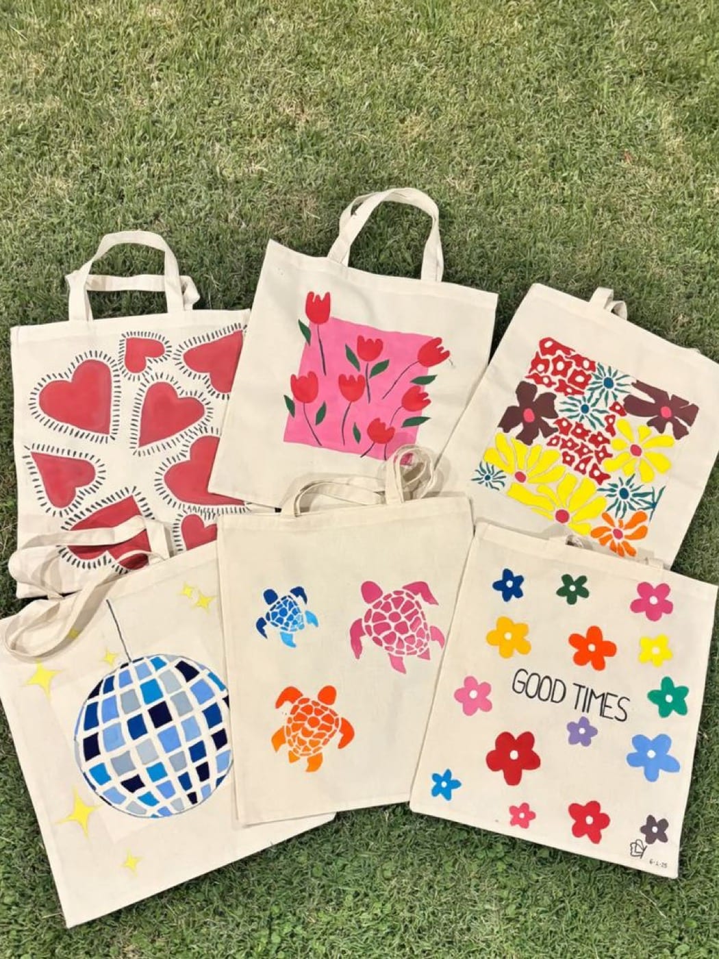Six tote bags personnalisés et colorés posés sur l’herbe