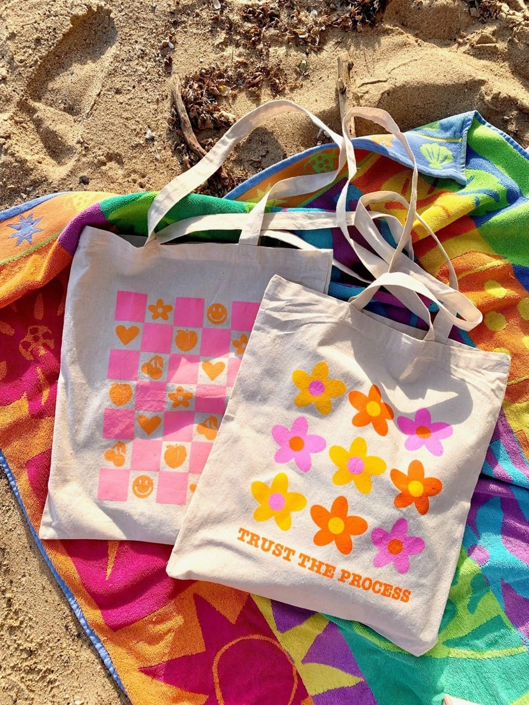 Deux tote bags personnalisés posés sur une serviette à la plage